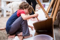 Garçon de sept ans utilisant un pinceau, carton à peindre — Photo de stock