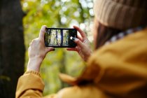 Woman holding up smart phone taking photograph of trees — Stock Photo