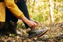 Закрытие женщины, сидящей на бревенчатом шнурке обуви на лесной дорожке — стоковое фото