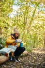 Frau sitzt auf Baumstamm im Wald und gießt Getränk aus Thermoskanne — Stockfoto
