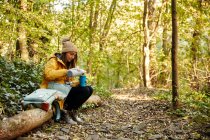 Женщина, сидящая на стволе дерева в лесу наливая напиток из термос фляжки — стоковое фото