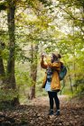 Mujer de pie en el camino del bosque tomando fotografías usando un teléfono inteligente - foto de stock