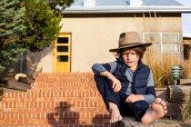 Портрет мальчика в шляпе-шляпе, расслабляющего на крыльце — стоковое фото