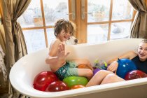 Jeune garçon et sa sœur aînée dans la baignoire remplie de ballons d'eau — Photo de stock