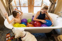 Young boy and his older sister in bathtub filled with water balloons — Stock Photo