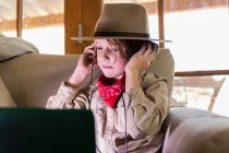 Jeune garçon en tenue safari et écouteurs regardant un film sur ordinateur portable — Photo de stock