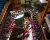Ragazzo seduto tra i giocattoli sul pavimento della sua camera da letto in una macchia di luce solare — Foto stock