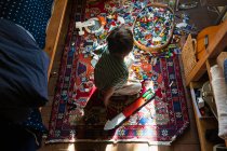 Junge sitzt zwischen Spielzeug auf dem Fußboden seines Schlafzimmers in einem Stück Sonnenlicht — Stockfoto