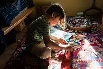 Menino sentado entre brinquedos no chão de seu quarto em um pedaço de luz solar — Fotografia de Stock