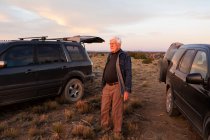 Senior man between SUV cars at sunset, Galisteo Basin, Santa Fe, NM — Stock Photo