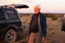 Senior man between SUV cars at sunset, Galisteo Basin, Santa Fe, NM — стоковое фото