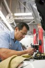 Mecânico hispânico inclinado em um motor de um carro em que ele trabalha em uma oficina de reparação de automóveis — Fotografia de Stock