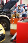 Mecánico hispano se inclina en un motor de un coche en el que trabaja en un taller de reparación de automóviles - foto de stock