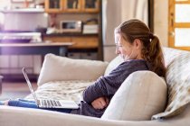 Дівчина-підліток дивиться на ноутбук на дивані — стокове фото