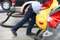 Mecánico de automóviles en un taller de reparación, apoyado en un coche, trabajando en él. - foto de stock