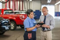 Männliche Pacific Islander Auto-Werkstatt Manager im Gespräch mit hispanischen Mechanikerin — Stockfoto