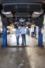 Two mechanics working on the underside of a care on a lift in a repair shop — Stock Photo