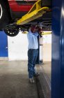 Mecánico en un taller de reparación trabajando en la parte inferior de un coche en un ascensor - foto de stock