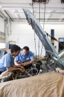 Mecânica masculina e feminina falando como eles olhando para o motor na oficina de reparação de automóveis — Fotografia de Stock