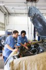 Mecânica masculina e feminina falando como eles olhando para o motor na oficina de reparação de automóveis — Fotografia de Stock