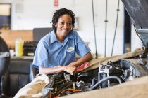 Retrato de sorridente mecânico feminino preto na oficina de reparação de automóveis — Fotografia de Stock