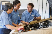 Drei Mechaniker teilen sich ein digitales Tablet und planen Reparaturarbeiten an einem Auto — Stockfoto