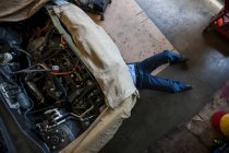 Meccanico che posa su un carrello sotto un'auto in un'officina di riparazione auto — Foto stock