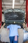 Torso de um mecânico inclinado para o compartimento do motor em uma oficina de reparação de automóveis — Fotografia de Stock