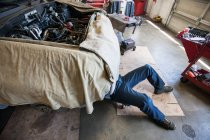 Mecánico que pone en un carro debajo de un coche en un taller de reparación de automóviles - foto de stock