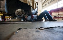 Mécanicien posé sur un chariot sous une voiture dans un atelier de réparation automobile — Photo de stock