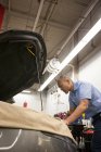 Mecánico de las islas del Pacífico apoyado en un coche mientras trabajaba en el compartimiento del motor en un taller de reparación de automóviles - foto de stock