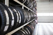 Longue rangée de pneus neufs sur un rack dans un atelier de réparation automobile — Photo de stock