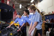 Drei Mechanikerinnen unterhalten sich beim Blick in den Motorraum eines Autos in einer Werkstatt — Stockfoto
