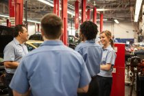 Equipo de mecánicos que trabajan en un coche discutir un problema en un taller de reparación de automóviles - foto de stock