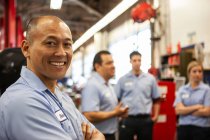 Portrait of smiling Pacific Islander repair shop owner with team in the background — Stock Photo