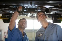 Two mechanics working on the underside of a car on a lift in a repair shop — Stock Photo