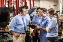Team of mechanics working on a car discussing a problem in an auto repair shop — Stock Photo
