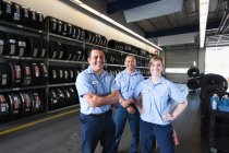 Retrato de mecánica sonriente en taller de reparación de automóviles, dos hombres y una mujer - foto de stock