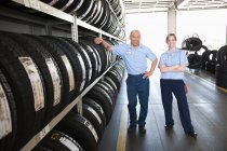 Portrait of smiling male and female mechanic by a rack of tires in a workshop — Stock Photo