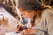 Teenagermädchen mit Wollmütze zeichnet mit Bleistift auf einem Skizzenblock. — Stockfoto
