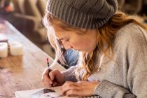 Adolescente en un sombrero de lana dibujando con un lápiz en un bloc de bocetos. - foto de stock