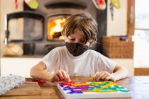 Young boy wearing mask playing board game at home — Stock Photo
