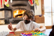 Мальчик в маске играет в настольную игру дома — стоковое фото