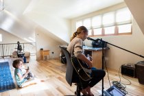 Четырнадцатилетняя девочка-подросток играет на гитаре и поет, ее брат играет на заднем плане — стоковое фото