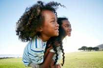 Young mixed race girl giving her younger brother a piggyback lift — Stock Photo