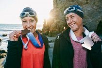 Zwei Schwestern, Triathleten, die in Badebekleidung, Bademütze und Brille ihre großen Medaillen tragen, Sieger. — Stockfoto
