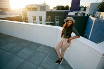 Young woman leaning on a parapet at sunset, city buildings in the background. — Stock Photo