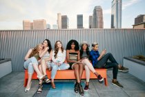 Grupo de mujeres jóvenes de fiesta en una azotea de la ciudad al atardecer - foto de stock