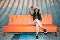 Joven mujer de raza mixta en un sombrero de panama sentado tomando una selfie, haciendo una cara - foto de stock