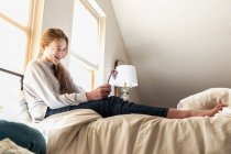 Дівчина-підліток лежить на її ліжку, використовуючи свій смартфон — стокове фото